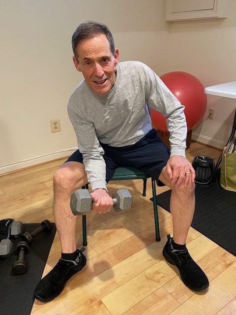 senior man sitting in chair doing bicep curl with dumbbell